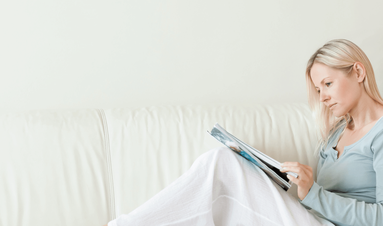 Frau liest Magazin auf weißem Sofa
